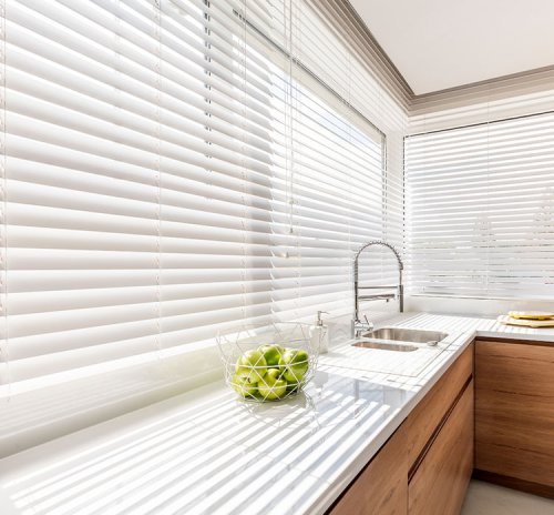 White 2 inch faux wood blinds reducing heat in a sunlit kitchen